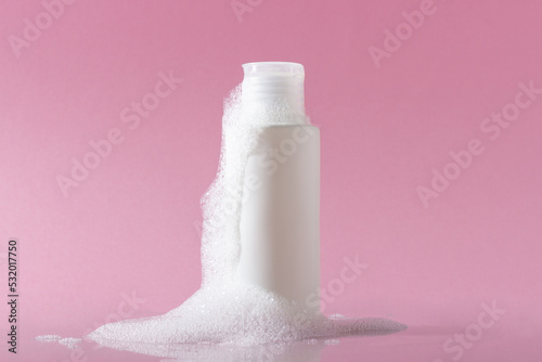 Cosmetics for face, body and hair care. Moisturizer, shampoo or facial cleanser on pink background with foam photo