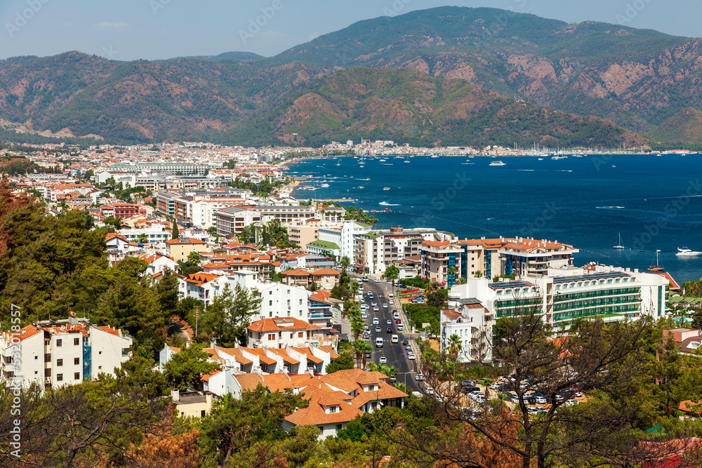 Marmaris, Turkey – View of the white houses with red roofs in the lively resort town of Marmaris with its green mountains at background of a sunny day against the blue sky and the Aegean Sea.
