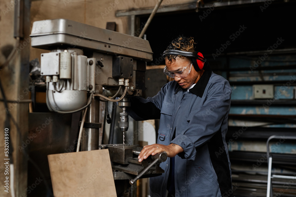 Waist up portrait of female worker operating machine unit and drilling metal in industrial workshop
