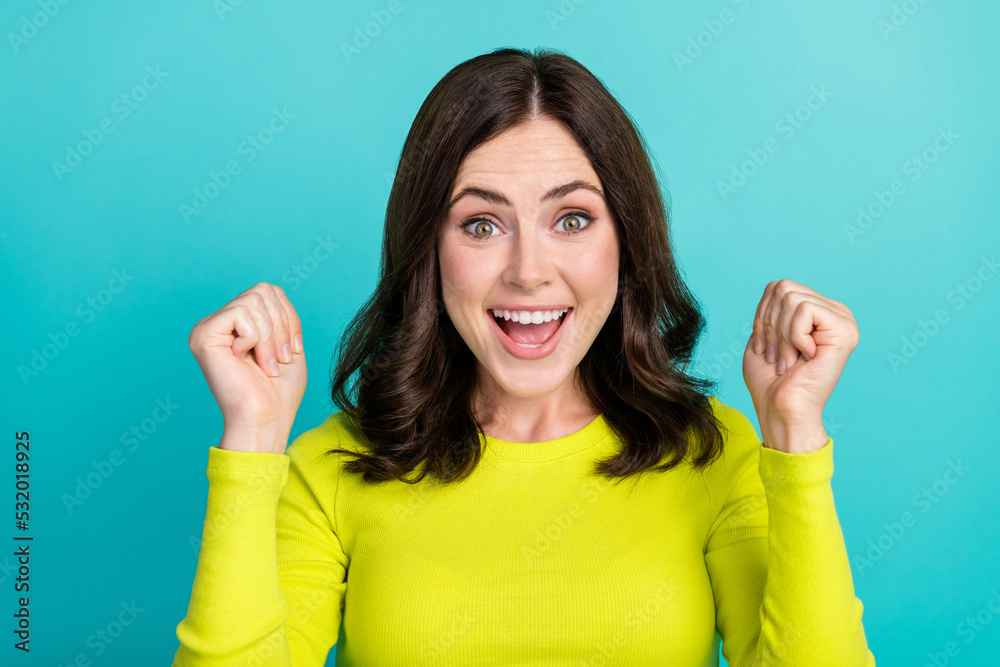 Closeup photo of young pretty cute woman wear lime pullover celebrate fists up smiling isolated on cyan color background Closeup photo of young pretty cute woman wear lime pullover celebrate fists up smiling isolated on cyan color background