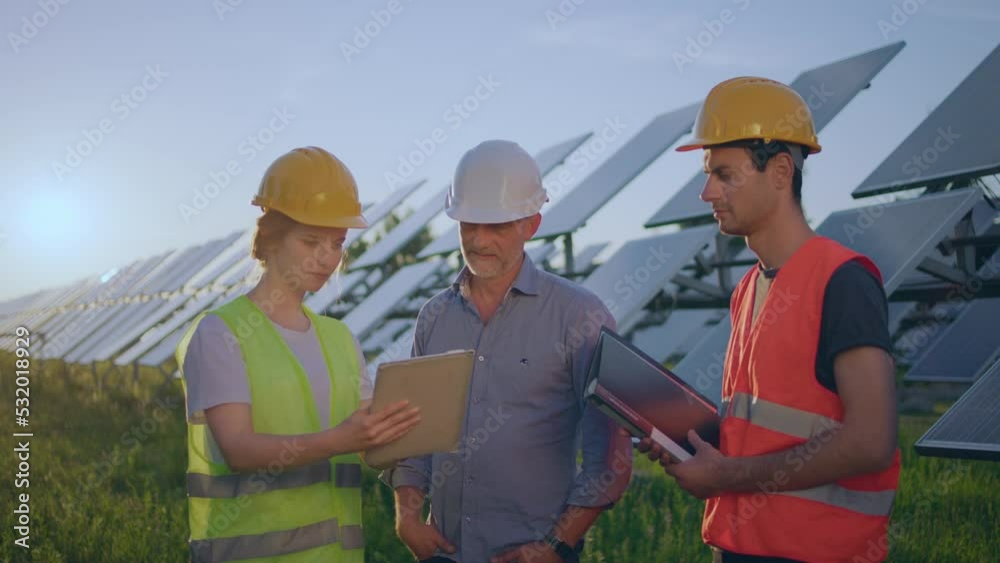 Charismatic group of investors and ecological engineer pretty woman all with safety helmets analysing the plan of work at photovoltaic solar panels farm. Shot on ARRI Alexa Mini Charismatic group of investors and ecological engineer pretty woman all with safety helmets analysing the plan of work at photovoltaic solar panels farm. Shot on ARRI Alexa Mini