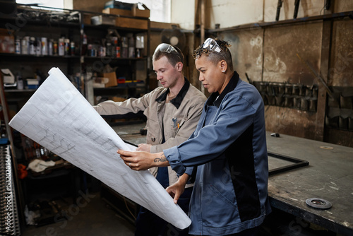 Side view portrait of two workers looking at blueprints in industrial factory workshop