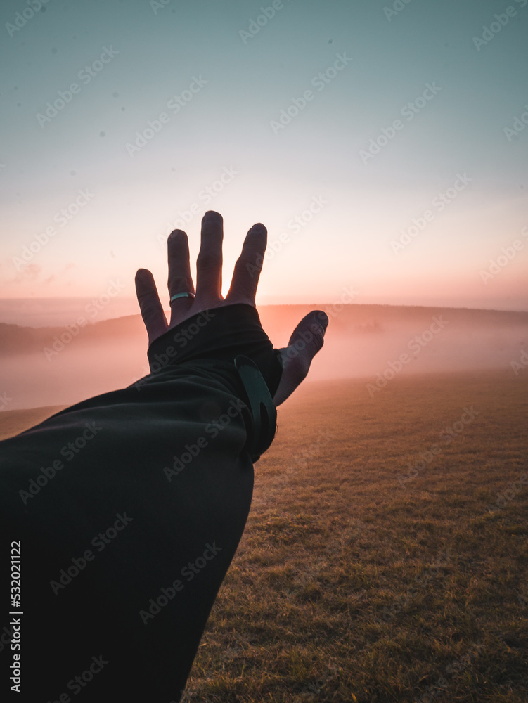 Hand catching sun at sunrise in fog in autumn