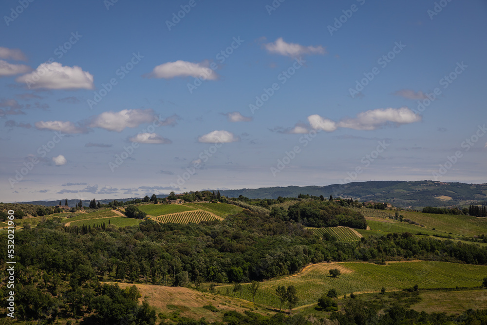 Rural view of Tuscany with rolling green hills and traditional Tuscan architecture on a partly sunny day.