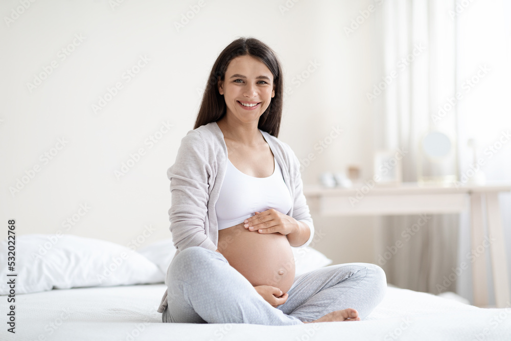 Beautiful pregnant woman sitting on bed at home Beautiful pregnant woman sitting on bed at home