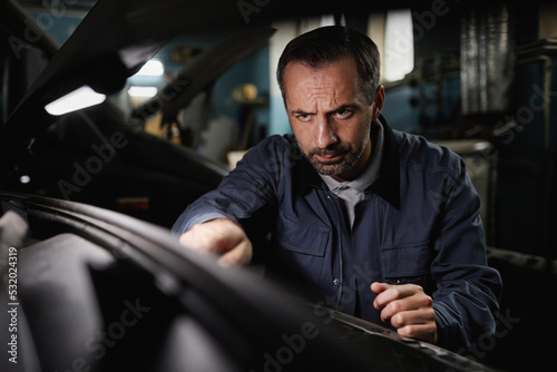 Portrait of mature car mechanic repairing engine in shop with intense face expression
