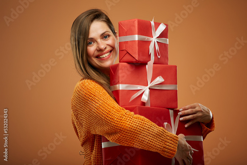 Happy woman holding stack of gift boxes. Isolated female portrait in christmas style on orange background.