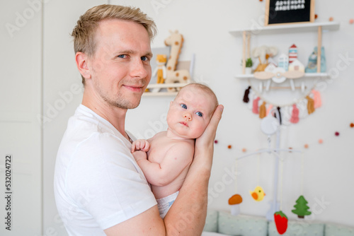 A young caucasian father gently holds a baby in a bright room at home. Happy fatherhood and the joy of being a father