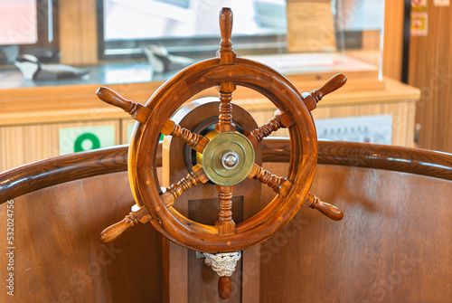 Close-up of a fake varnished wooden ship's wheel called a helm steered by a helmsman tied with a sailor's coil knot and used to change the rudder's angle so that the pirate's ship can turn on the sea. photo