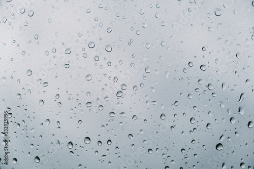 Raindrops flow down by the window glass. Rainy weather. Gray cloudy sky background. Sad depressed mood. Nature cry concept. Autumn weather detail. Wet and cold season. Abstract texture. Grey texture