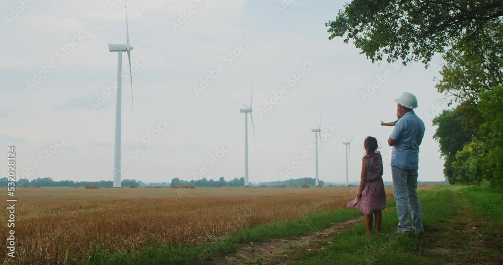 Young engineer father with children holding his daughter hand and little son in his arms, the father showing the windmill field. Renewable energy concept, love for nature, family Young engineer father with children holding his daughter hand and little son in his arms, the father showing the windmill field. Renewable energy concept, love for nature, family