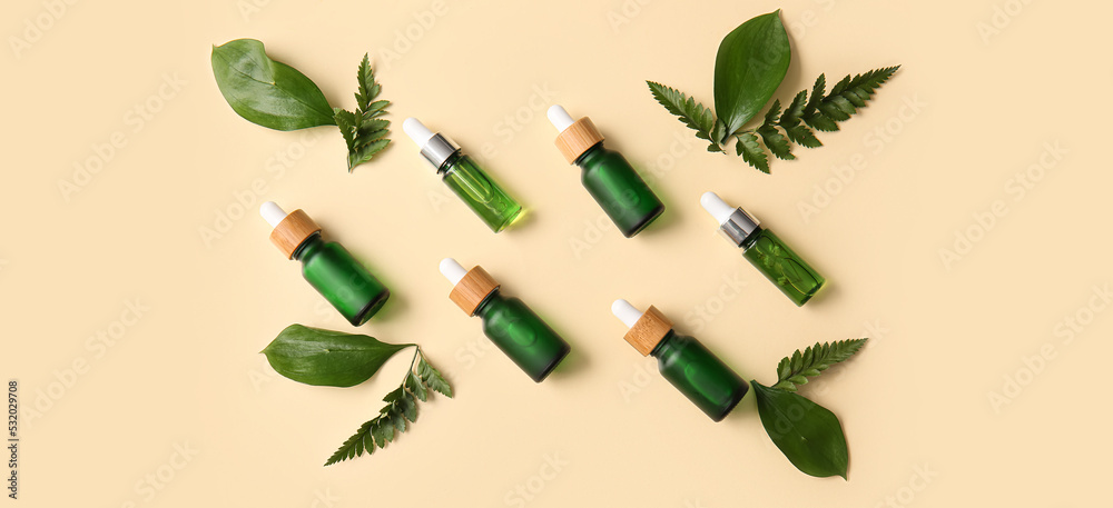 Different bottles of cosmetic serum and green leaves on beige background, top view Different bottles of cosmetic serum and green leaves on beige background, top view