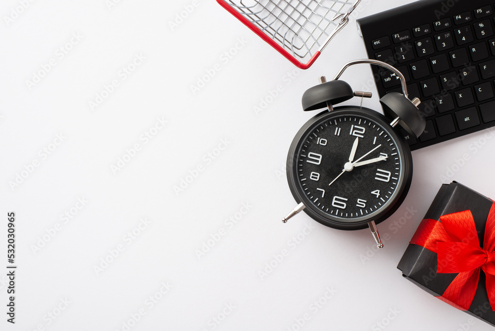 Cyber monday concept. Top view photo of alarm clock shopping cart keyboard and giftbox with red ribbon bow on isolated white background with empty space Cyber monday concept. Top view photo of alarm clock shopping cart keyboard and giftbox with red ribbon bow on isolated white background with empty space