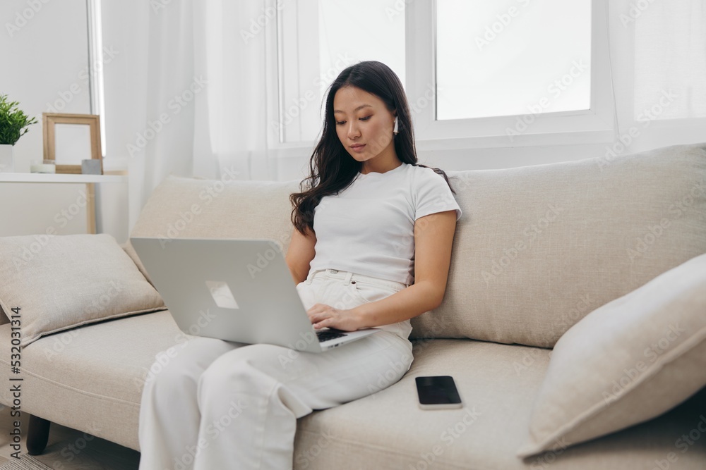 Asian woman sitting with laptop and phone in freelancer's home office looking at laptop screen with headphones working, lifestyle work and home Asian woman sitting with laptop and phone in freelancer's home office looking at laptop screen with headphones working, lifestyle work and home