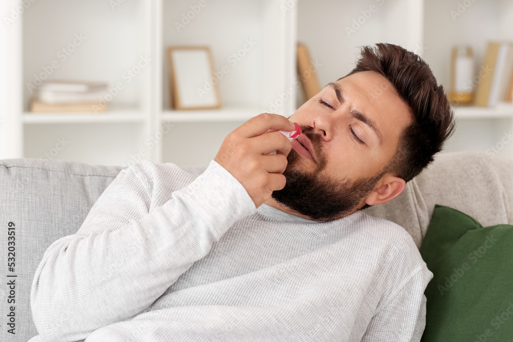 Young bearded man with nosebleed and tissue at home Young bearded man with nosebleed and tissue at home