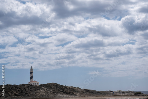 panorama of Favaritx lighthouse, with a rock formation around it on a cloudy summer day, horizontal, copy space, Menorca, Balearic Islands, Spain