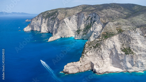 Drone view to boat in crystal pacific blue sea and impressive cliffs on idyllic beautiful greek island