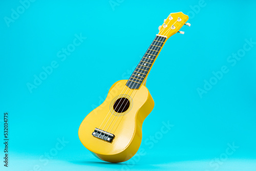 Perspective photo of ukulele with central composition. Yellow colored wooden ukulele guitar on the turquoise blue background. photo