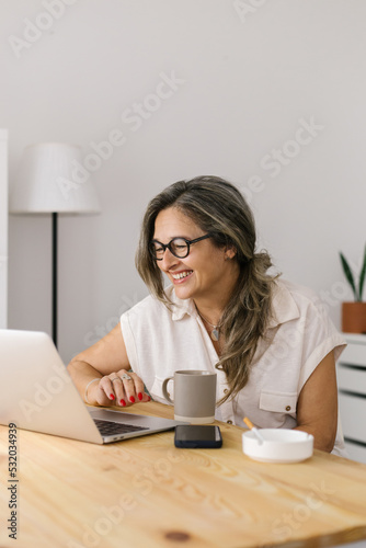 Smiling woman having online meeting at home via laptop
