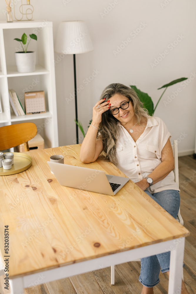 Smiling woman sitting and working from home via laptop Smiling woman sitting and working from home via laptop