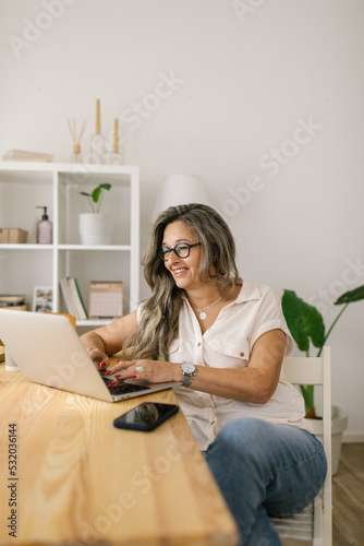 Happy woman texting on social media via laptop at home