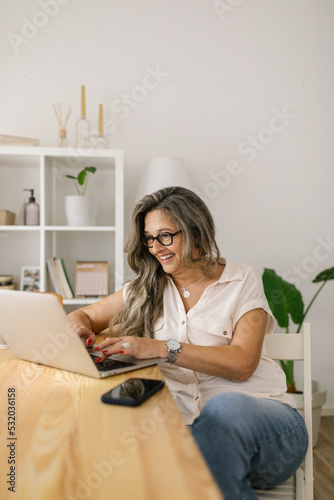 Happy female texting on social media via laptop at home