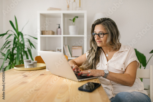 Mature woman texting on social media via laptop at home