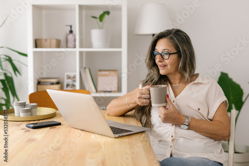 Woman holding cup of coffee and looking at the computer