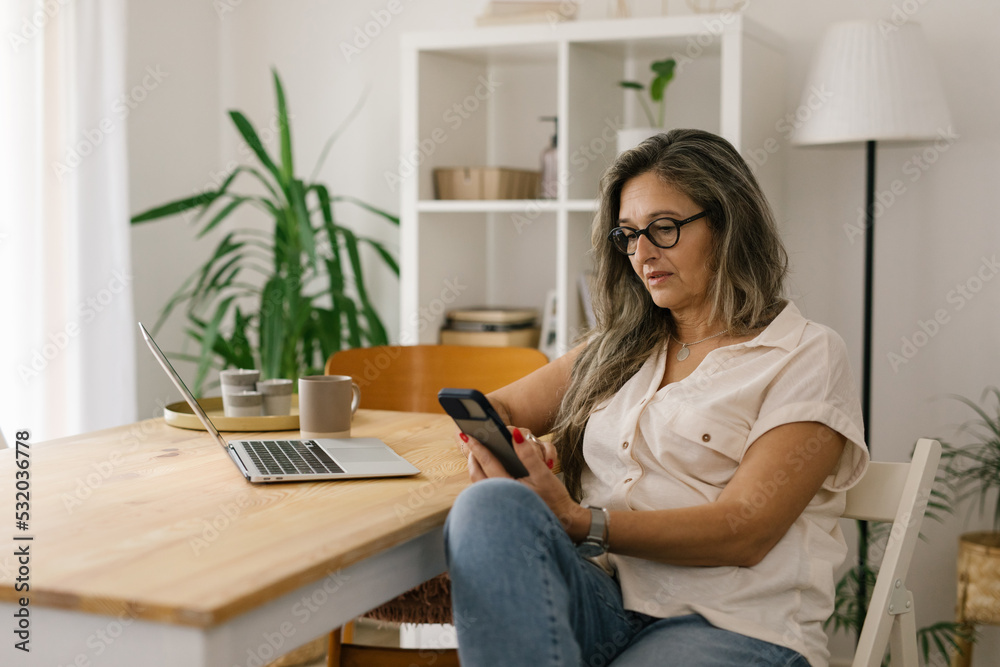 Mature woman sitting and using cellphone at home Mature woman sitting and using cellphone at home
