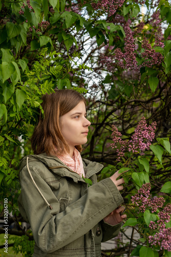 Portrait of a young teenage girl in the garden, a bush of blooming lilacs in the spring. High quality photo