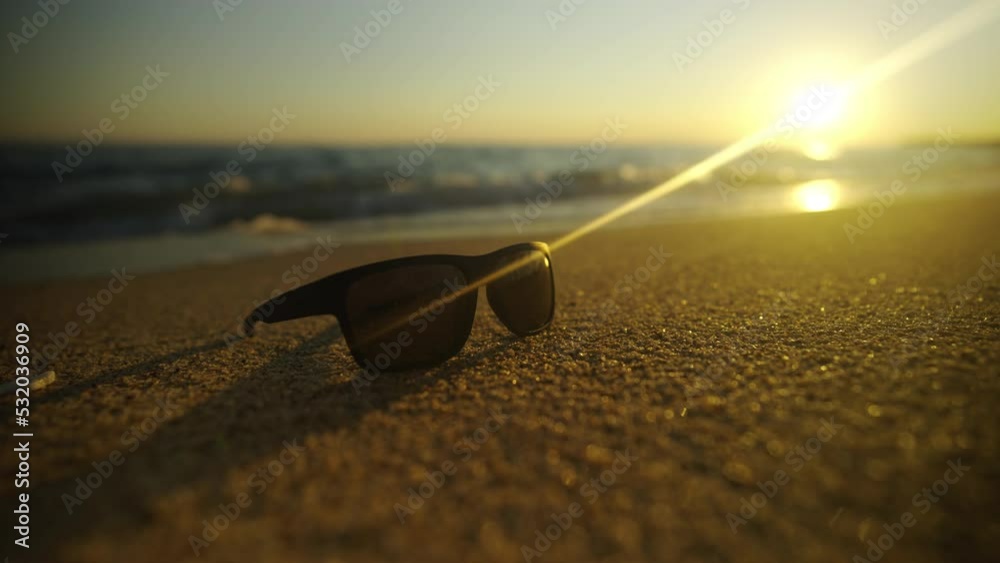 Sunglass on the beach sand at sunset. Waves floating on the sand and golden sun in the sky background