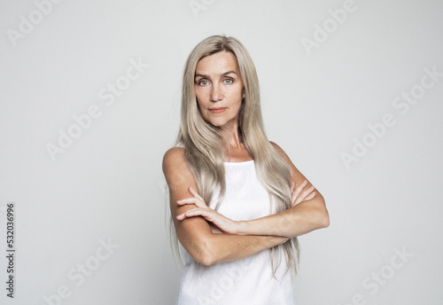 Mature elderly woman standing with arms folded over grey background. © Raisa Kanareva