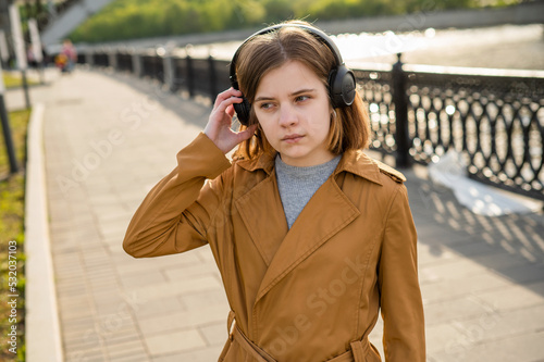 Young teenage girl listens to music in headphones, walks along the embankment in the city. High quality photo