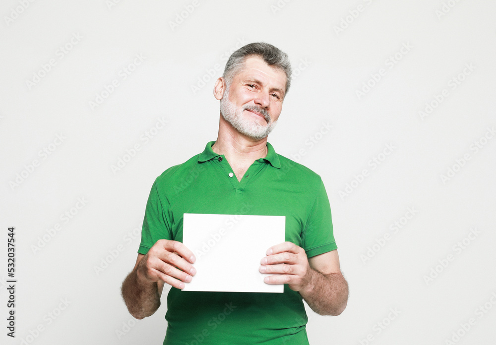 Senior handsome man with mustache and beard wearing green shirt holds the white sign in a studio Senior handsome man with mustache and beard wearing green shirt holds the white sign in a studio
