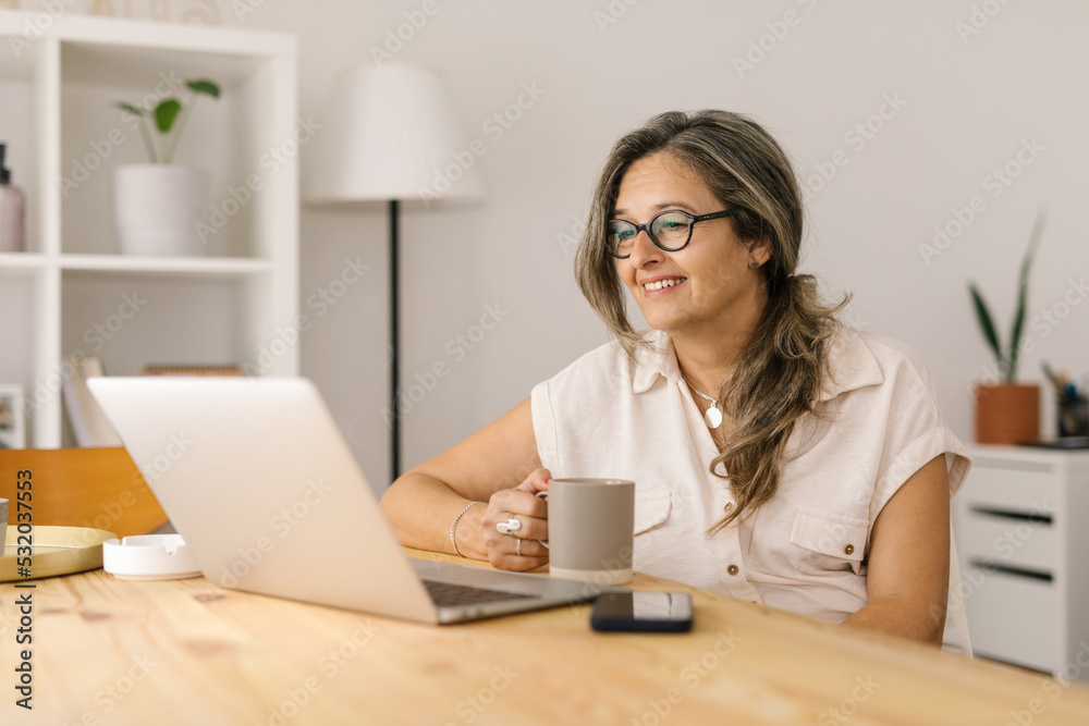 Woman holding a cup and reading from computer screen Woman holding a cup and reading from computer screen