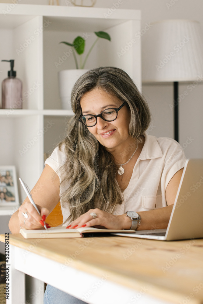 Happy woman writing down in notebook with pen at home