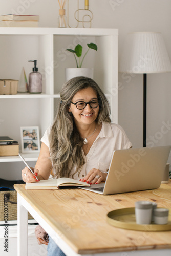 Mature happy female taking notes from online meeting