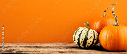 Decorative pumpkins on wooden table on orange background. Harvest, Thanksgiving Day banner design. photo