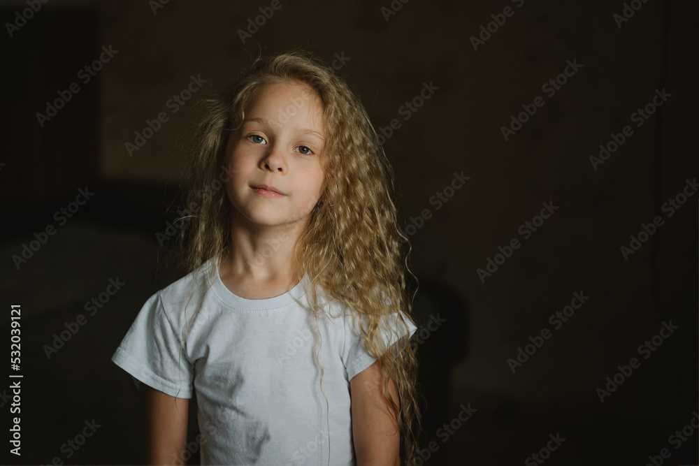 close-up portrait of a little blonde girl with long curly hair with a calm emotion on a dark background, looking at the camera close-up portrait of a little blonde girl with long curly hair with a calm emotion on a dark background, looking at the camera