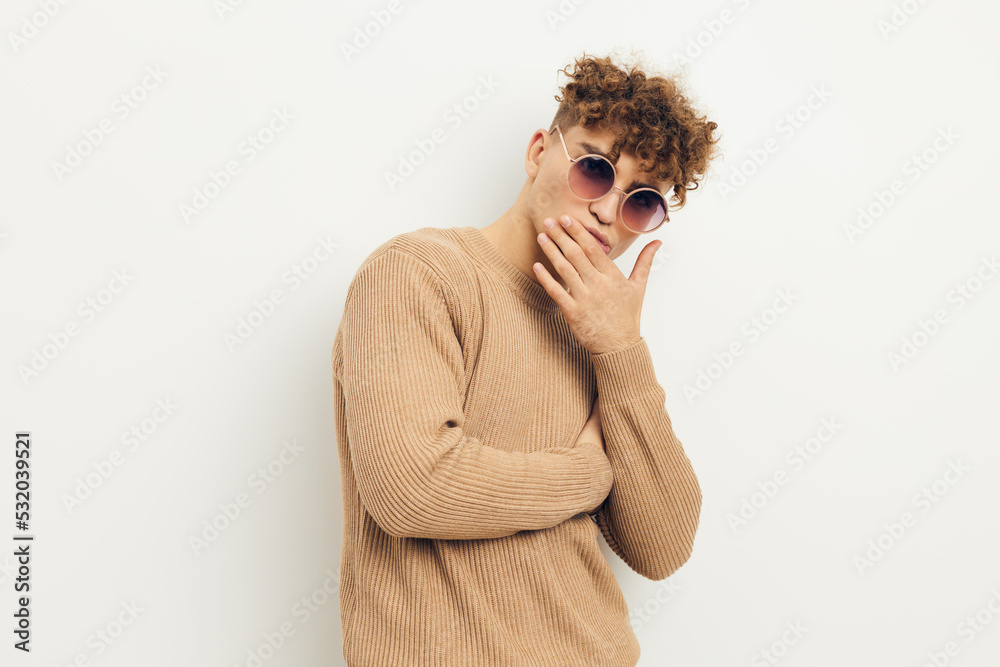 horizontal photo of a handsome, handsome man standing on a light background in beige clothes with round sunglasses holding his hand near his face horizontal photo of a handsome, handsome man standing on a light background in beige clothes with round sunglasses holding his hand near his face