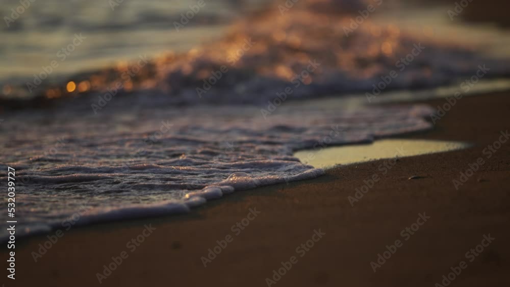 Sea waves rolling in slow-motion on empty sandy beach at sunset