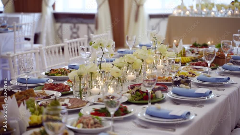 Wedding rustic style decor with dishes, drinks and roses in white and blue colours on table setting at restaurant. Banquet hall interior floristic details with flowers in glass vases filled with water Wedding rustic style decor with dishes, drinks and roses in white and blue colours on table setting at restaurant. Banquet hall interior floristic details with flowers in glass vases filled with water