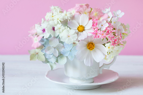 Colorful bouquet with hydrangea, cosmos flower, phlox in a cup on a white table on a pink background. Greeting card for the holiday. © tachinskamarina