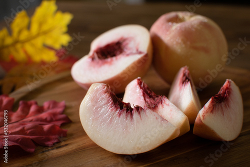 Organic White Peach with Peaches Sliced Next to it on Wooden Table and Dark Background. Fresh Fruit with Beads of Water and Fall and Autumn Leaves.