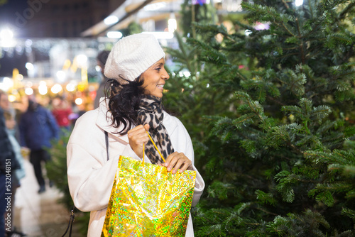 Smiling Latin American woman who came to an open-air Christmas fair chooses a Christmas tree