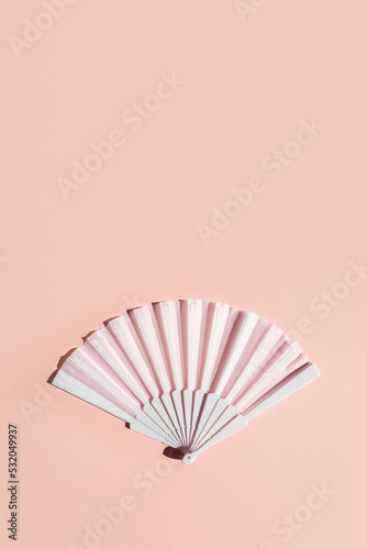 White fan on beige background with hard shadows. Minimal concept of menopause and female hot flashes. Vertical banner, copy space