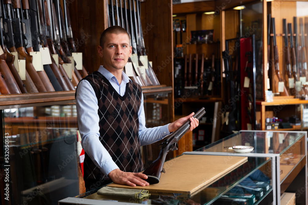 Φωτογραφία Confident owner of the gun shop demonstrates a rare collectible hunting rifle
