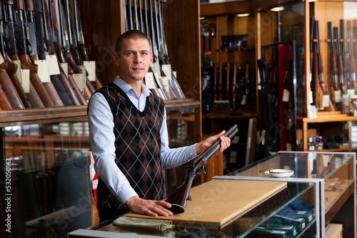 Confident owner of the gun shop demonstrates a rare collectible hunting rifle © JackF