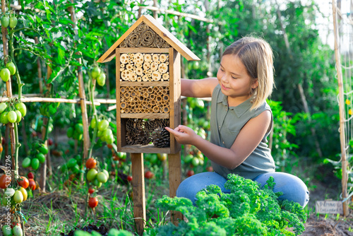Portrait of happy girl next to hotel for insects in of wooden birdhouse in the garden © JackF