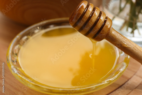 Delicious honey flowing down from dipper into bowl on wooden table, closeup